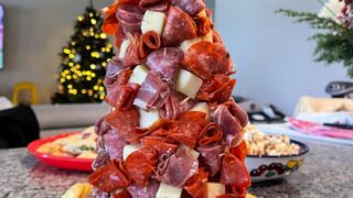 A tree filled with cheese and meat, surrounded by Ritz crackers, with a star on top and the words "Charcuterie Tree For Christmas" digitally written on top.