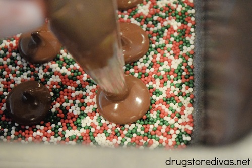 Melted chocolate being piped onto red, white, and green sprinkles in a bread pan.