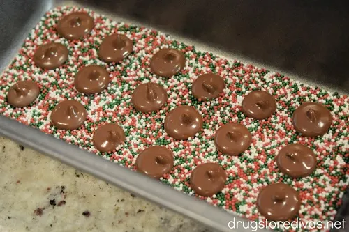 A bunch of homemade chocolate nonpareils on top of red, white, and green sprinkles in a bread pan.