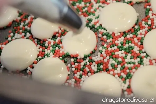 Melted white chocolate being piped onto red, white, and green sprinkles in a bread pan.