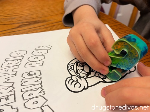 Two small hands, one using an S crayon, to color on a coloring book.