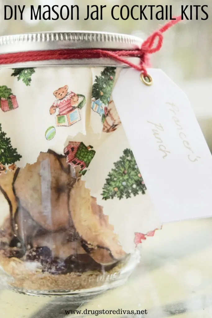 A mason jar with dried fruit in it, Christmas fabric on it, and a gift tag with the words "DIY Mason Jar Cocktail Kit" digitally written up top.