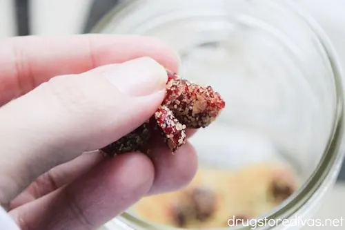 A hand adding candied craisins into a mason jar.