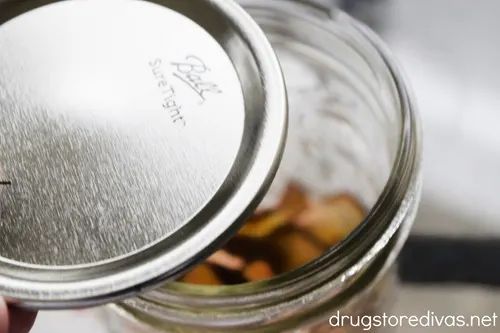 A mason jar lid being placed on top of a filled jar.
