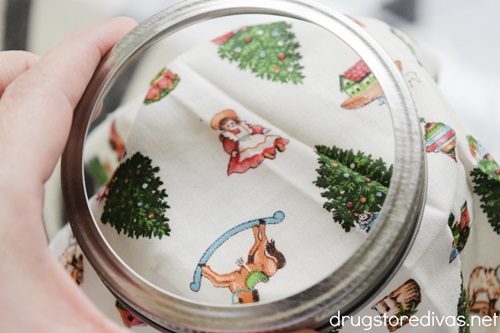 A mason jar cap being put on top of Christmas fabric.