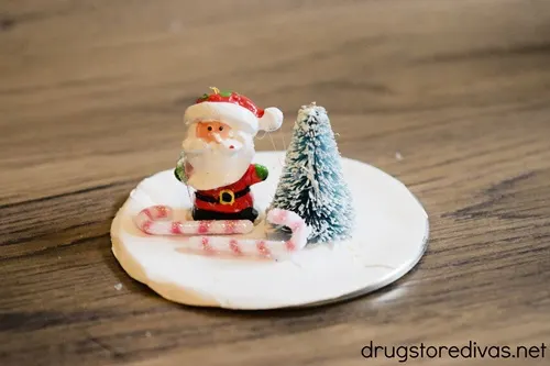 A Santa, tree, and two candy canes on a white paper on a mason jar lid.