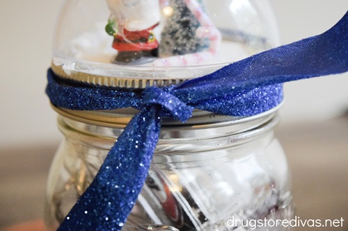 A blue ribbon tied between a snow globe lid and a mason jar.