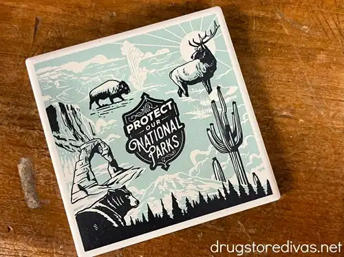 A blue, white, and black coaster with a deer and cactus and some other cartoon images on it that says "Protect Our National Parks."