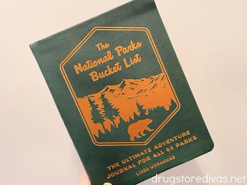 A green book called "The National Parks Bucket List" being held up by a hand.