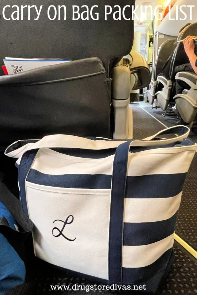 A blue and white striped tote bag with an L on it with an airplane aisle and seats behind it with the words "Carry On Bag Packing List" digitally written on top.