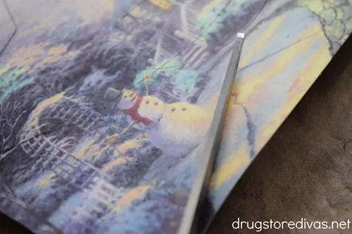 A pair of scissors cutting a card with a winter scene on it.
