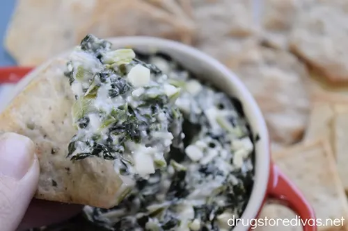Spanakopita dip in a red mini Dutch oven surrounded by crackers with a cracker coming out of the dip with dip on it.