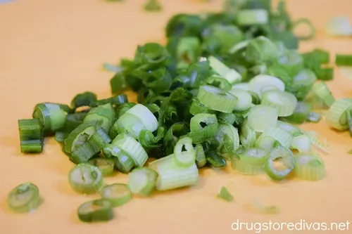 Cut green onions on an orange cutting board.