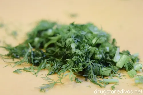 Chopped dill on an orange cutting board.