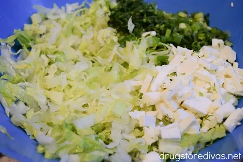 Chopped lettuce, dill, green onions, and feta cheese in a blue bowl.