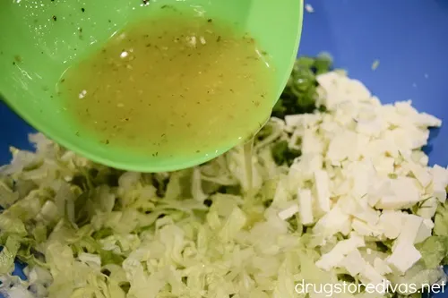 A green bowl with dressing being poured over salad in a blue bowl.