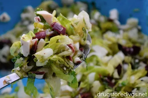 A spoon holding Maroulosalata with Olives over a bowl of salad.