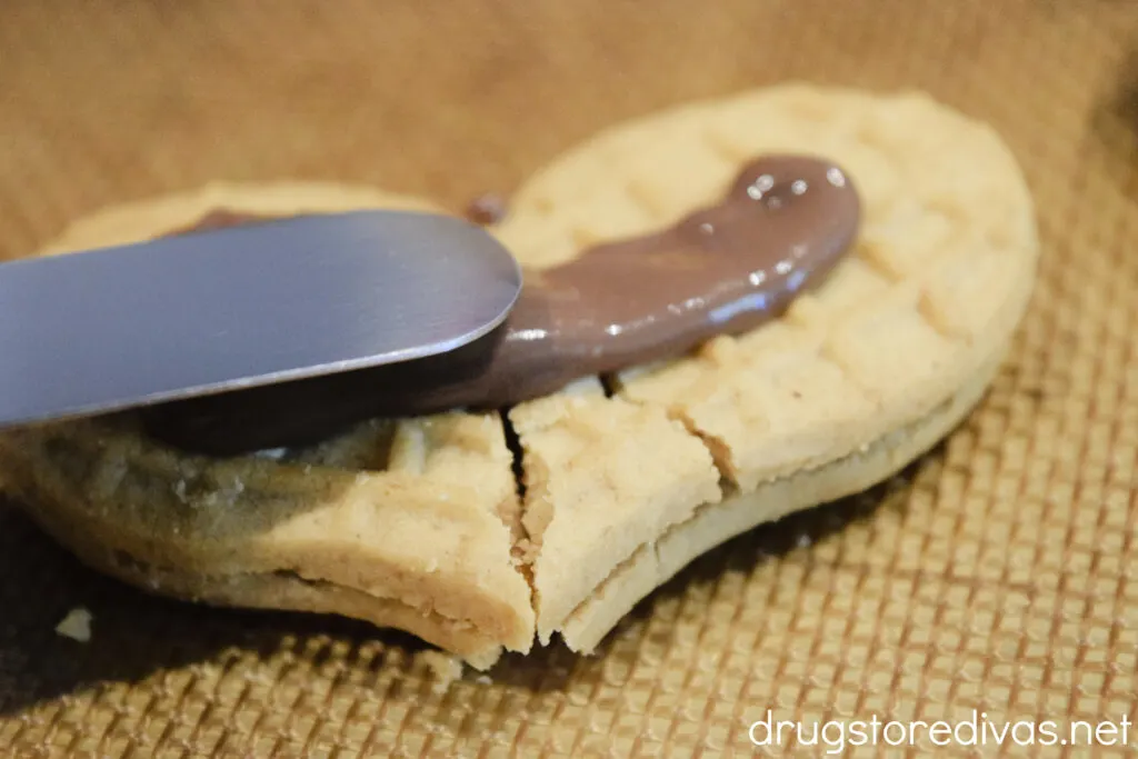 An icing spatula spreading melted chocolate on a Nutter Butter cookie.