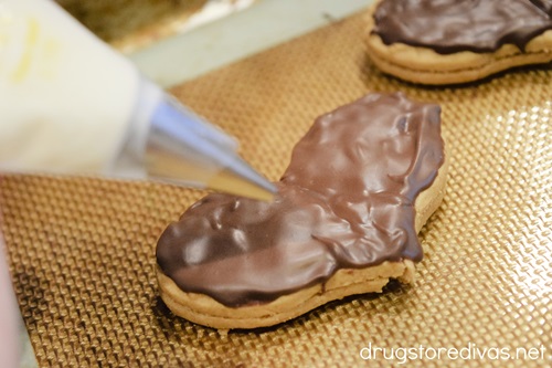 Melted white chocolate in a piping bag over a chocolate-covered heart cookie.