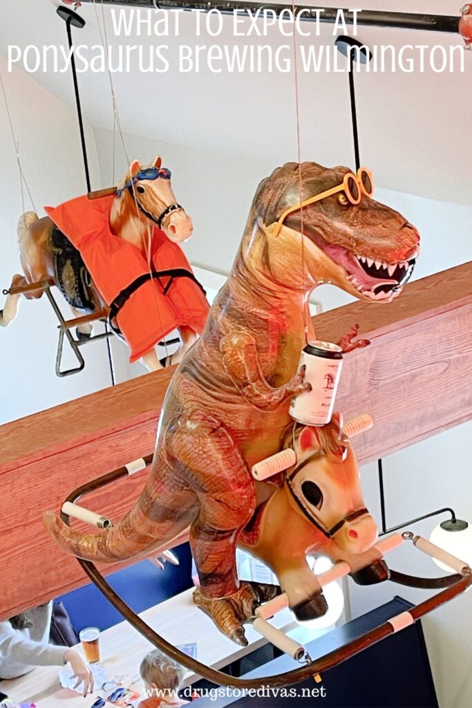A carousel horse wearing a life preserver and an inflatable T-Rex holding a beer on a children's ride on toy horse, both suspended from the ceiling, with the words "What To Expect At Ponysauraus Brewing Wilmington" digitally written on top.