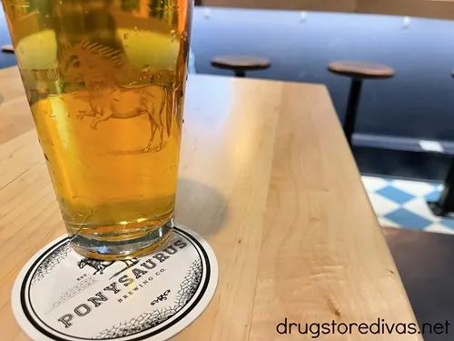 A beer on top of a Ponysaurus coaster on a table.