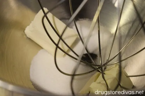 Cream cheese and sugar in a silver bowl with a whisk attachment down into them.