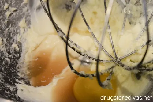 A thick cream and vanilla extract in a silver bowl with a whisk attachment down into them.