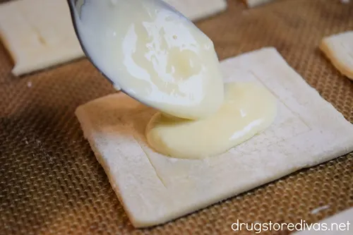 A spoon putting filling onto a puff pastry rectangle.