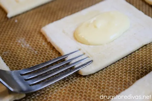 A fork making indents around the edge of a rectangle of puff pastry that's filled with cream.