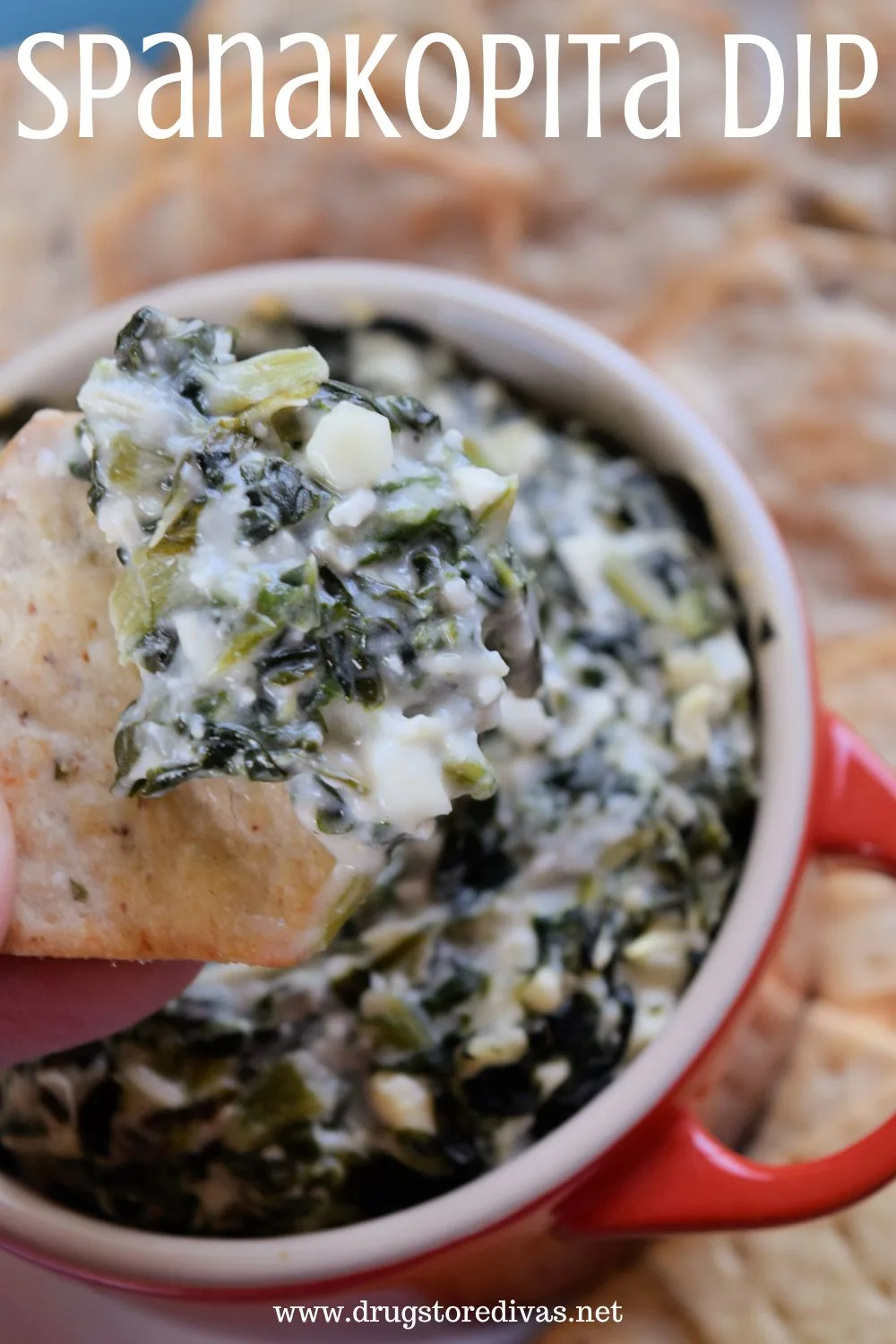 A chip with dip on it over a red ramekin of dip surrounded by crackers and the words 