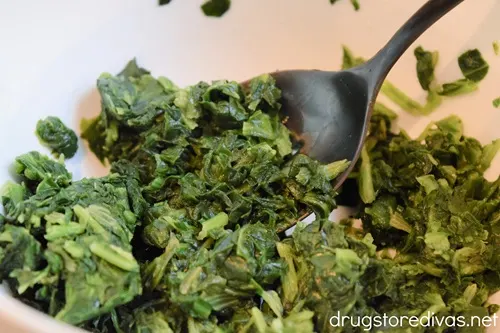 Spinach in a white bowl with a mixing spoon.