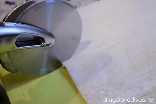 A pizza wheel cutting a puff pastry sheet.