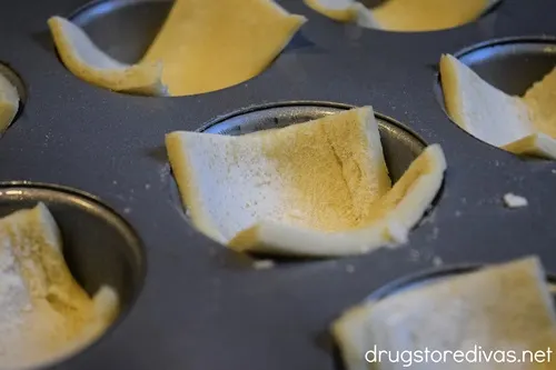 Pieces of puff pastry in muffin pan cavities.