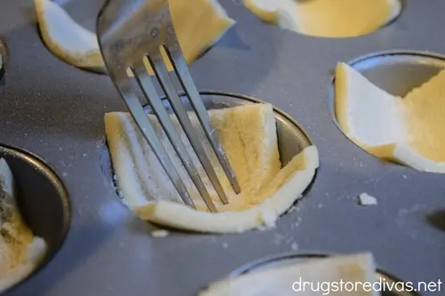 A fork in a pieces of puff pastry in a muffin pan cavity.