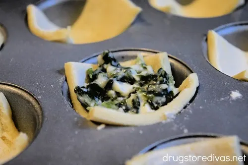 Pieces of puff pastry with spanakopita filling in muffin pan cavities.