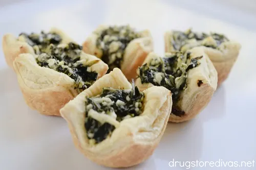 Six spanakopita puff pastry bites on a white tray.
