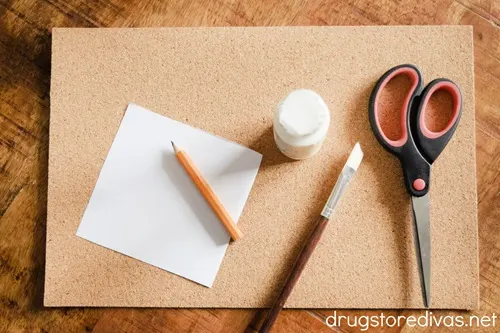 A piece of cork paper, a white paper square, a golf pencil, white acrylic paint, a paint brush, and scissors.