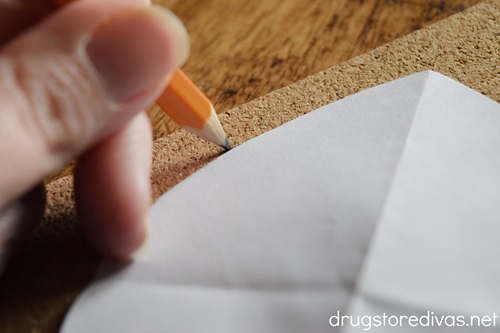 A white piece of paper being traced with a pencil onto cork paper.