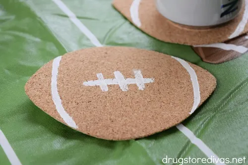 A football coaster on a football tablecloth with another coaster and a can on top in the background.