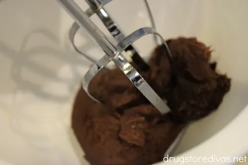 Two hand mixer beaters on top of chocolate frosting in a white bowl.