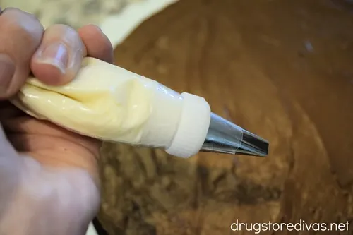 White frosting in a piping bag that's over a football-shaped brownie.