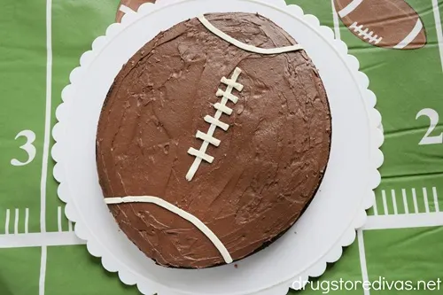 A football-shaped brownie on a white plate with scalloped edges on a football-themed tablecloth