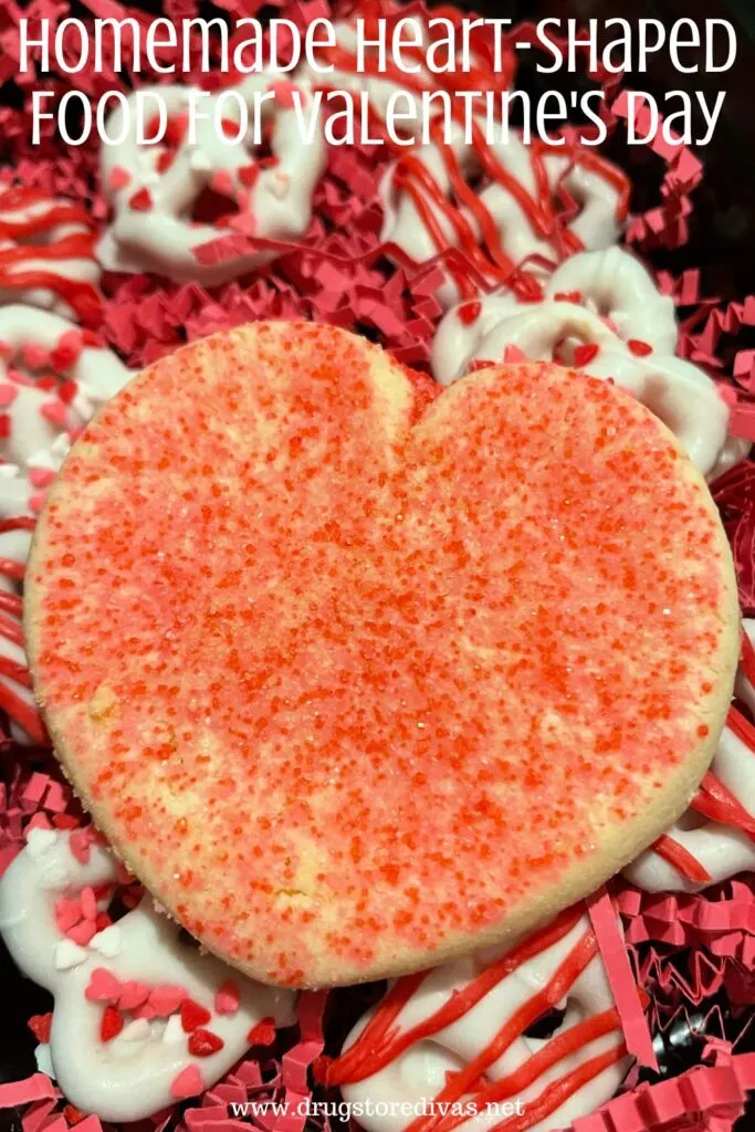 A heart shaped cookie with pretzels and pink paper shred behind it with the words "Homemade Heart-Shaped Foods For Valentine's Day" digitally written on top.