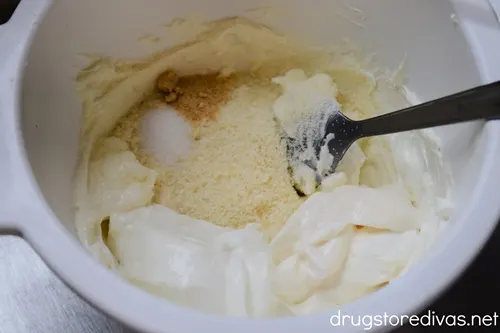 Cream cheese, sour cream, parmesan cheese, mayo, and seasoning in a white bowl with a spoon.