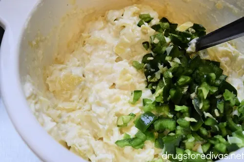 Artichoke dip with sliced jalapeno peppers on the side of the bowl.