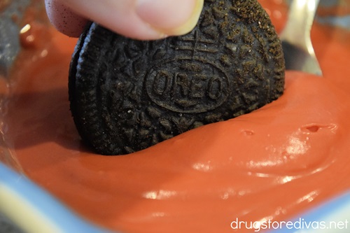 An OREO cookie being dipped into red candy melts.