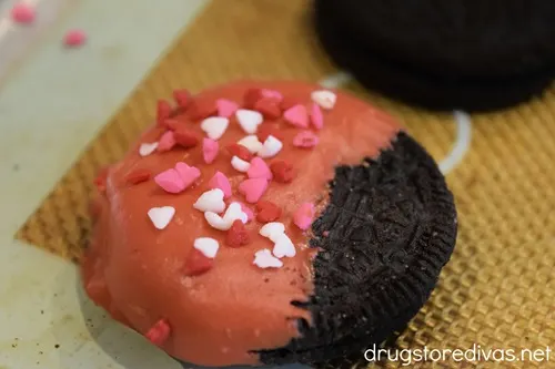 A red dipped OREO cookie with heart-shaped sprinkles on it.