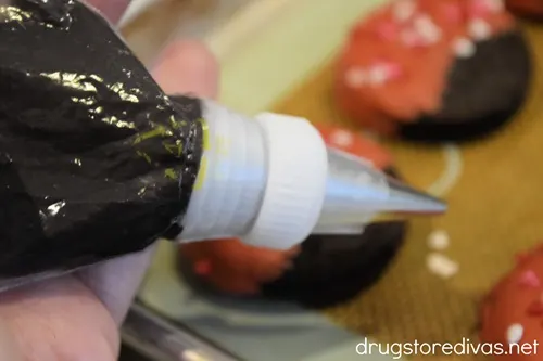 A piping bag with black candy melts in it over a tray of ladybug cookies.
