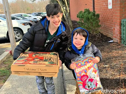 Two young boys, one is holding two pizzas and the other is holding a goody bag from Chuck E Cheese.