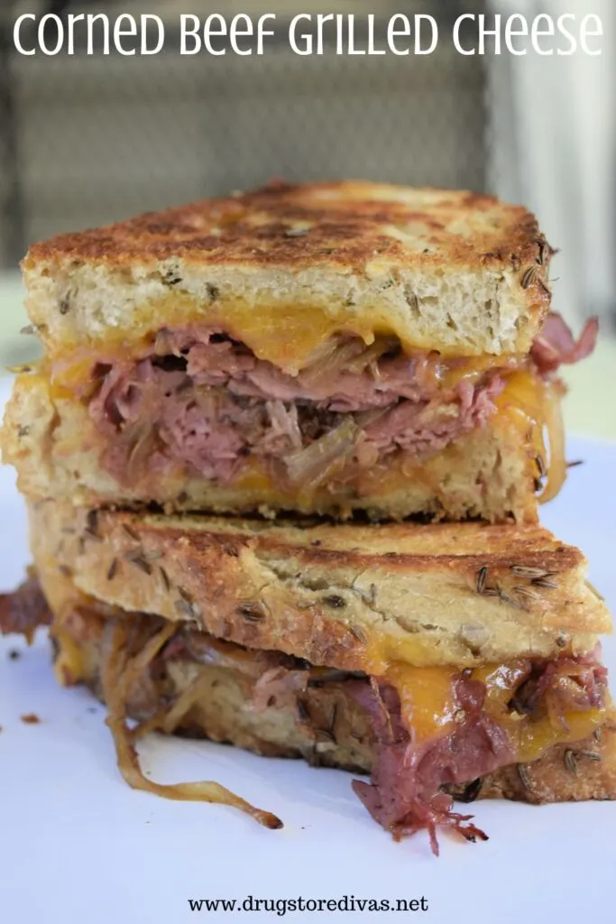 Two halves of a corned beef and cheese sandwich on top of each other with the words "Corned Beef Grilled Cheese" digitally written on top.